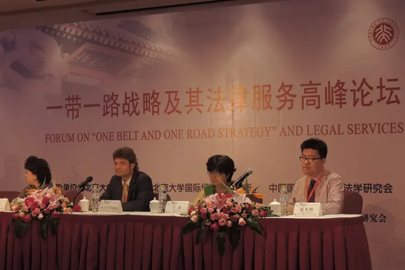 Panel discussion at the Forum on “One Belt and One Road Strategy and Legal Services” with five speakers seated behind a table adorned with floral arrangements. The backdrop displays Chinese characters and the English forum title. ICLA is represented on stage.
