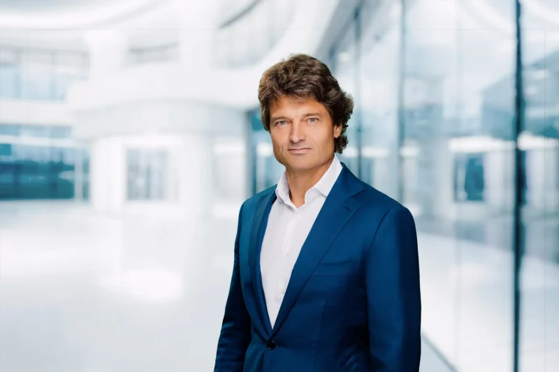 Portrait of Dr. jur Wolfgang Breyer in a modern, brightly lit office interior with glass walls and soft reflections.